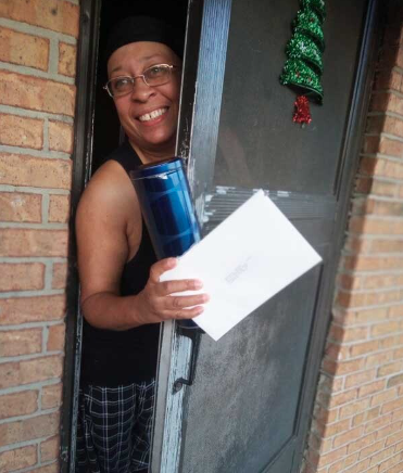 A resident has her head through the open door crack and is smiling as she holds on to her gift and an envelope. 