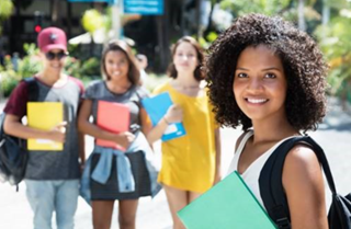 A young woman holding a book with her fellow students standing behind her. 