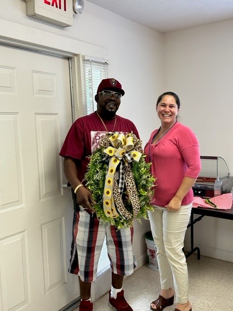 A man and a woman pose with a flower wreath.
