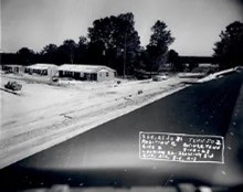 A road covered in snow with houses and trees in the background.