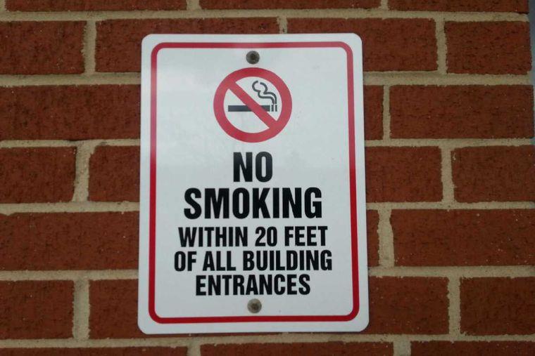 No Smoking within twenty feet of all building entrances sign on a brick wall.