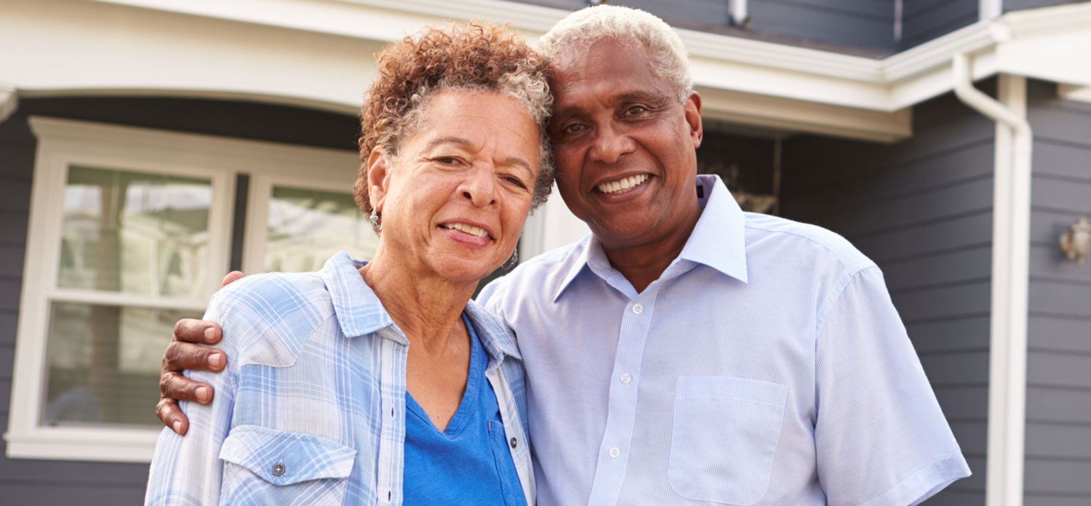 Elderly couple standing in front of house