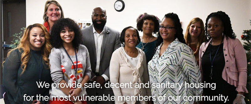 A group of people standing together with text that reads: We provide safe, decent and sanitary housing for the most vulnerable members of our community.