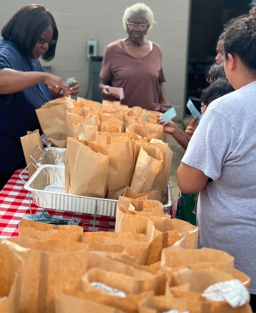 People standing around a table getting lunch at the 2024 Family Fun Day Back-to-School Bash.