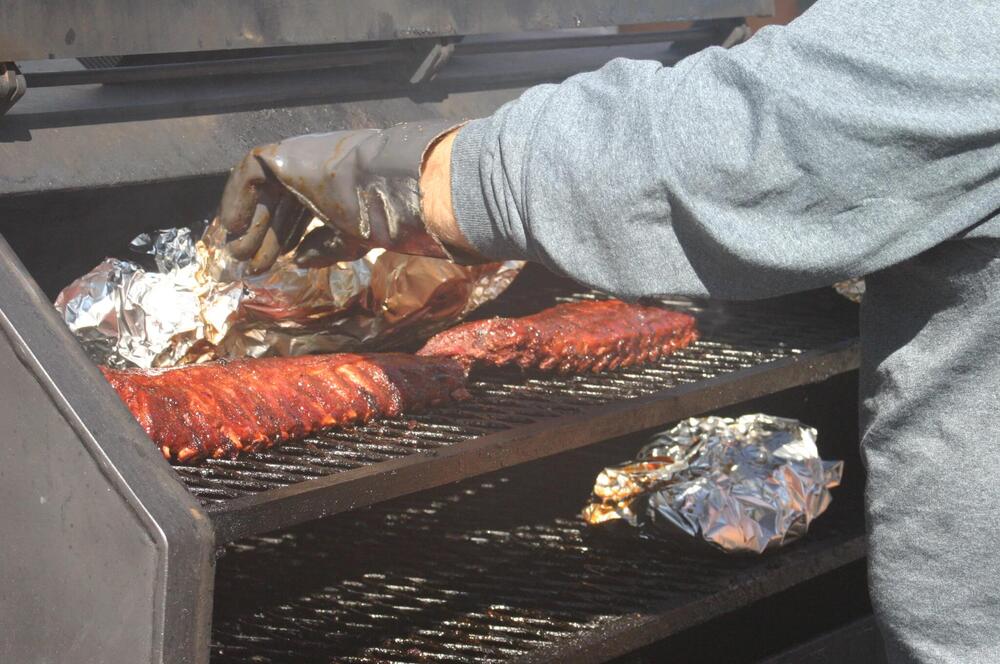 A person taking tin foil off of the ribs on the grill.