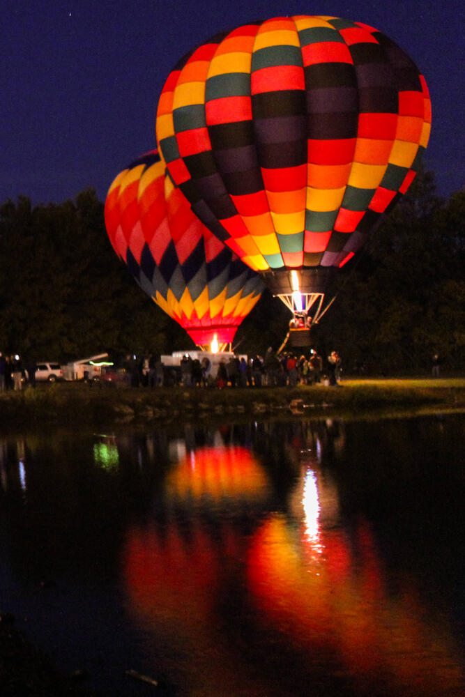 Two hot air balloons near the water at night.