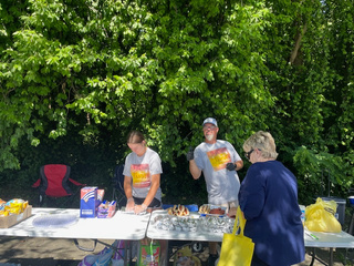 Two people serving food on a table outside