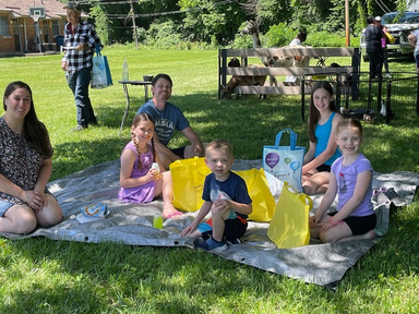 A group of people sitting on a tarp on the grass.