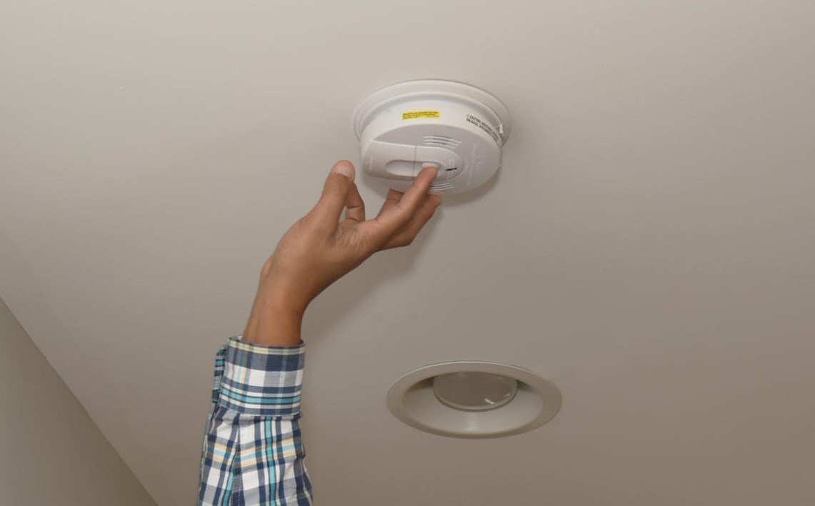 Hand pushing a button on a smoke detector. 