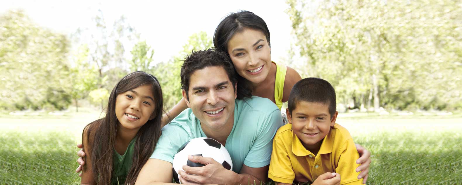 Family of four laying on the ground with the dad holding a soccer ball.