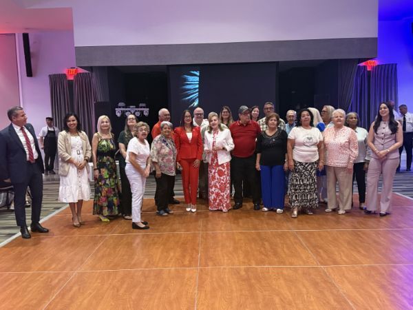 A group of 23 people stand and smile for a photo on the dancefloor.