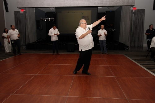 A man standing in the middle of the dance floor with a microphone pointing to another man.