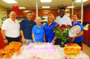 Individuals gathering around a table with a birthday cake.