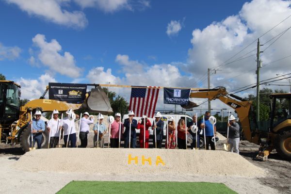 A large group of people holding shovels and wearing hard hats to break ground.
