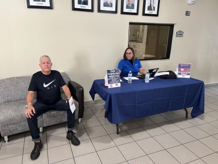 Man sitting on a couch next to the voter registration table with english and spanish information.