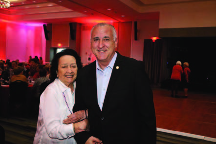 A man dressed in a suit standing next to a woman, both of them smiling.