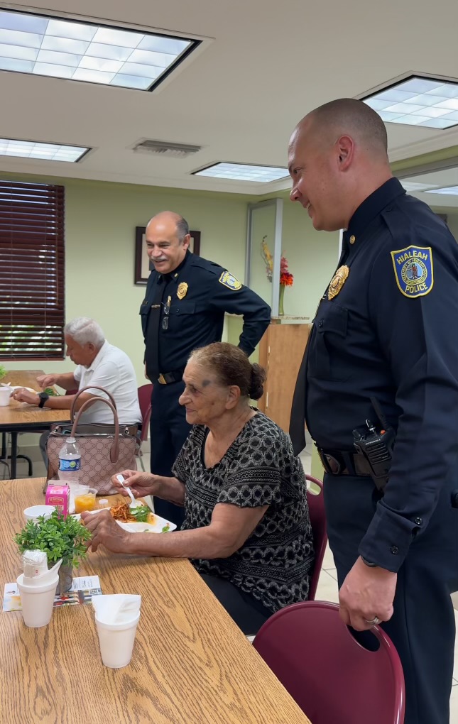 Two officers standing around a lady seated at a table.