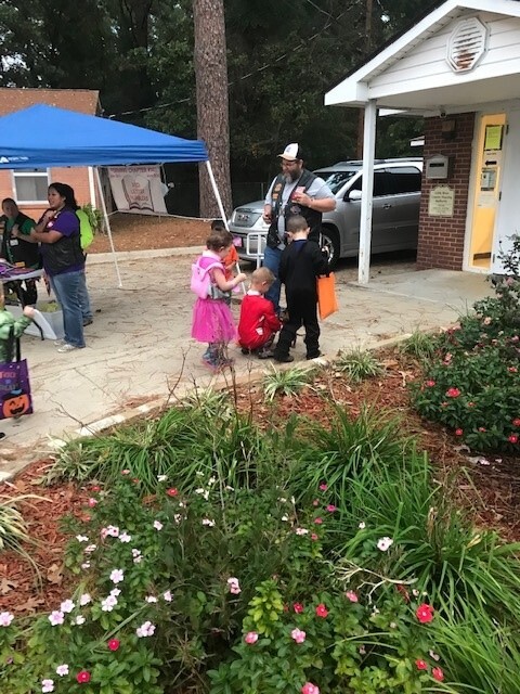 Kids getting candy from a biker while trick or treating. Adults under a canopy.