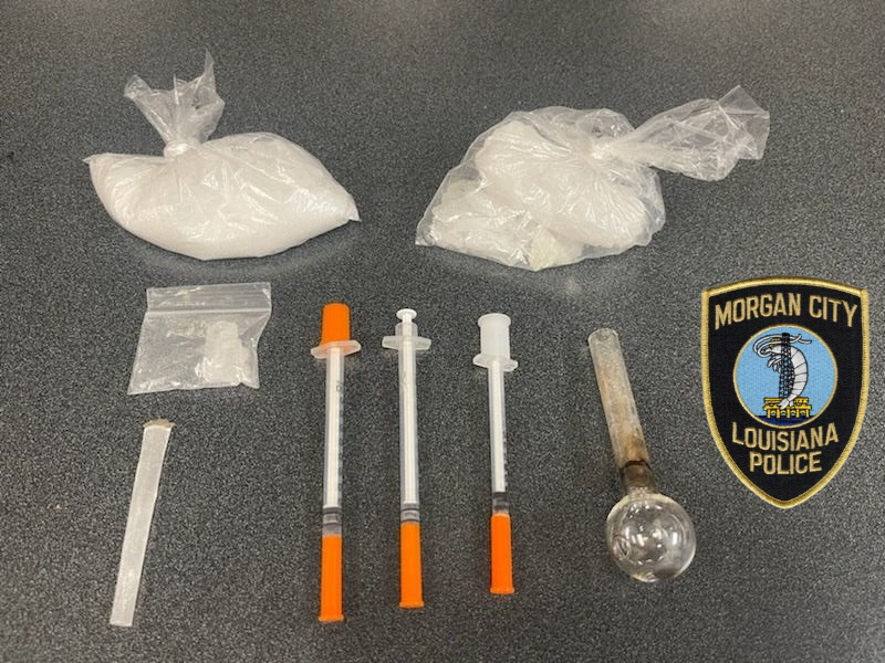 Bags of white powder, needles, a pipe on a table with the Morgan City Police Department patch. 