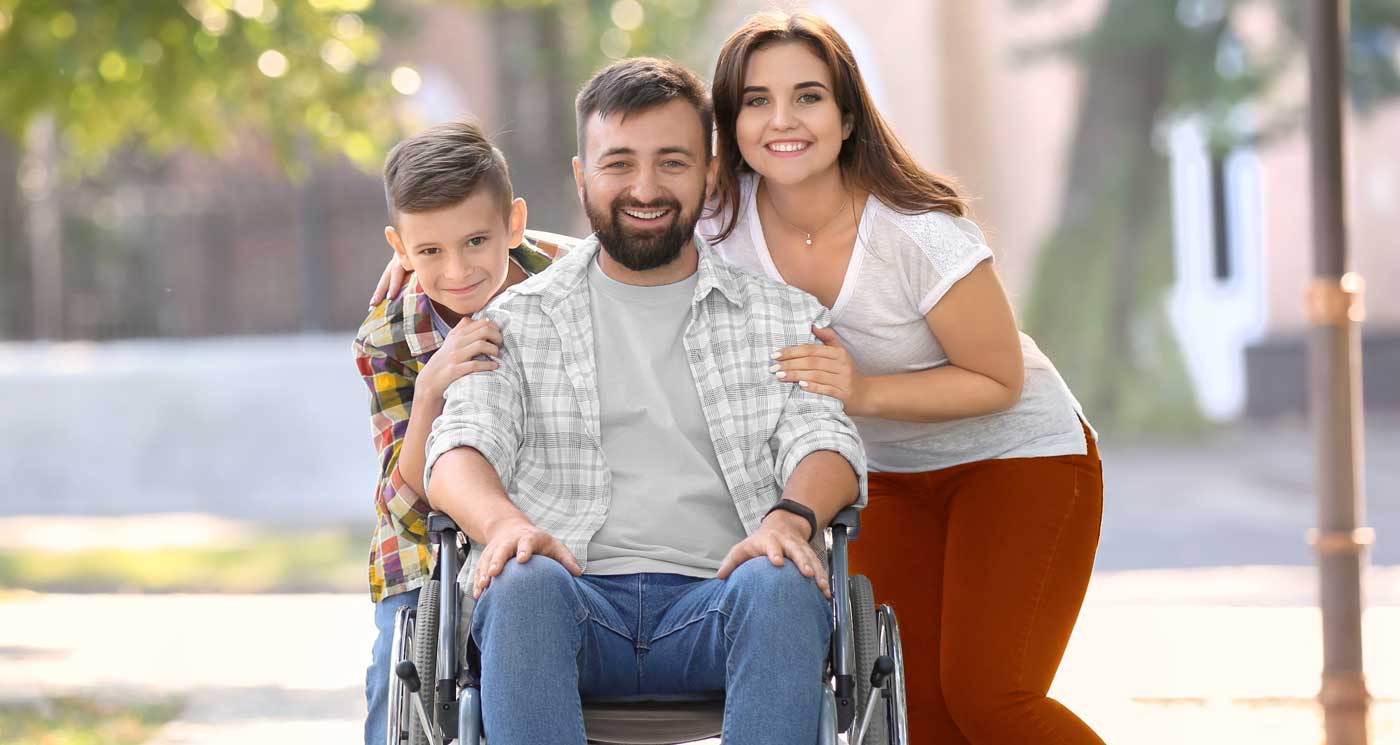 A young boy and mother posing with father in a wheelchair