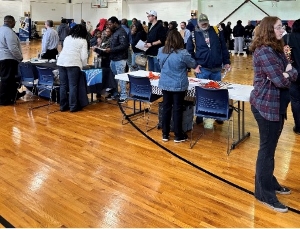 Groups of people standing at and around table in an auditorium.