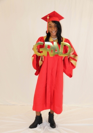 Ms. Garrett in her cap and gown holding a GRAD sign.