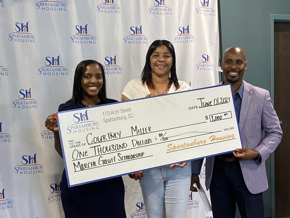 Three people smiling holding a scholarship, with Courtney Miller in the middle.