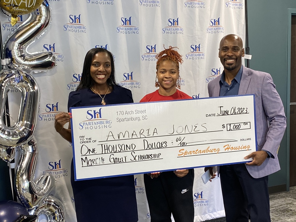Amaria Jones smiling while holding her scholarship check, with 2 other people.