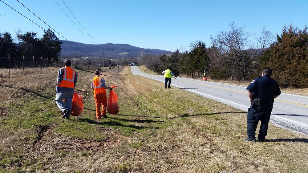 A member of the Sheriff's office overseeing an inmate road crew cleaning up the side of a road.
