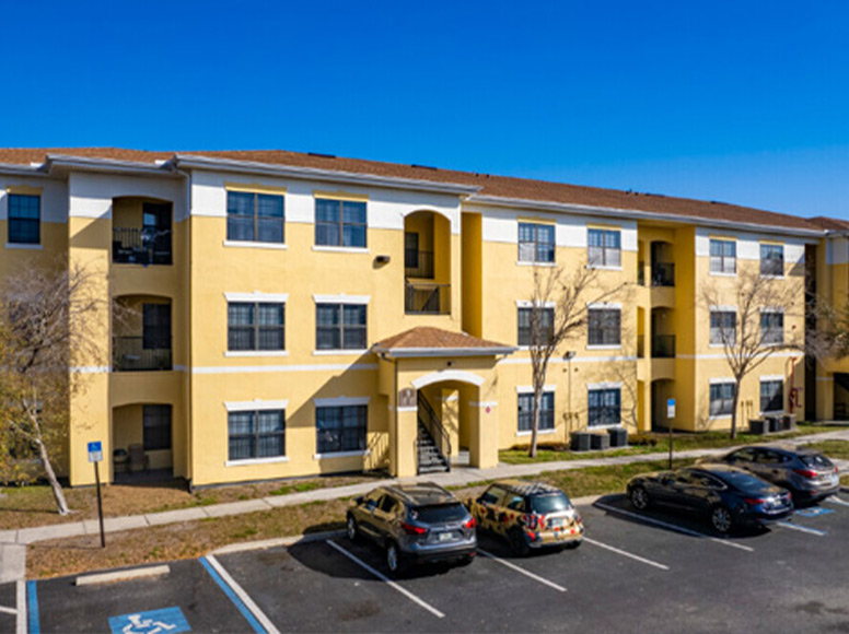 A yellow building with a large parking lot.