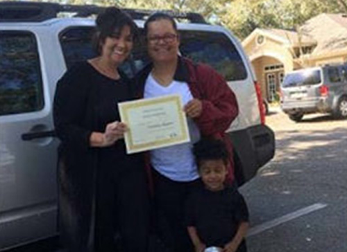 Two women standing outside holding an award, with a child standing beside them.