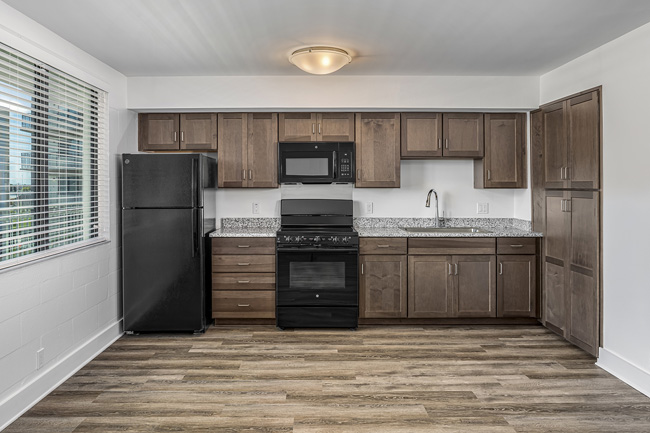 A kitchen with black colored appliances and wood flooring.