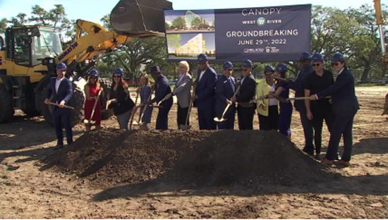 Individuals standing in line with shovels and a pile of dirt.