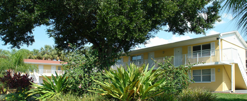 Yellow apartment building surrounded by trees, on a sunny day.