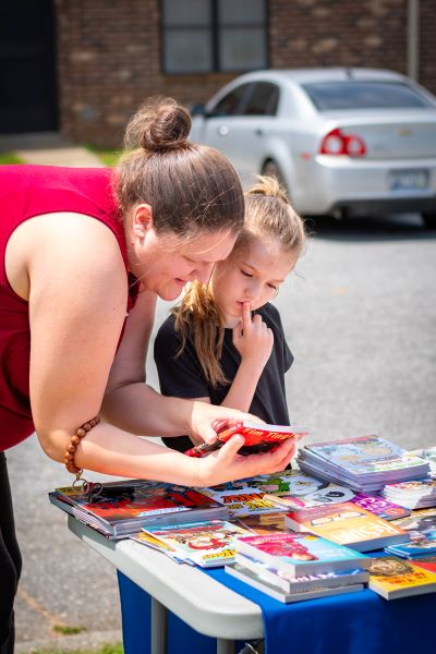 A woman is helping a girl pick out a book. 