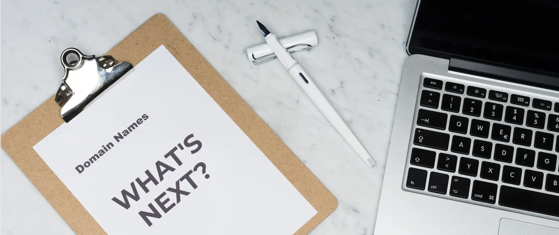 A white printer paper on a clipboard beside a silver laptop used by The Talking Owl to represent What’s Next After Purchasing a Domain Name