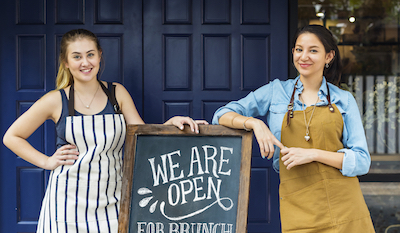 Cheerful business owners standing with open blackboard New Businesses Wanted