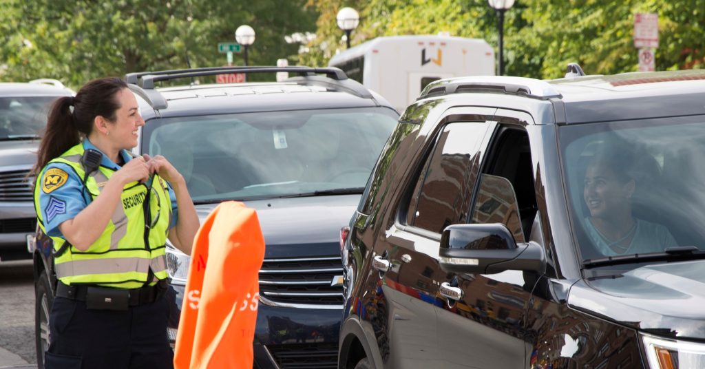 Cars lined up parked next to orange-bagged meters and a DPSS Security officer welcoming their arrival