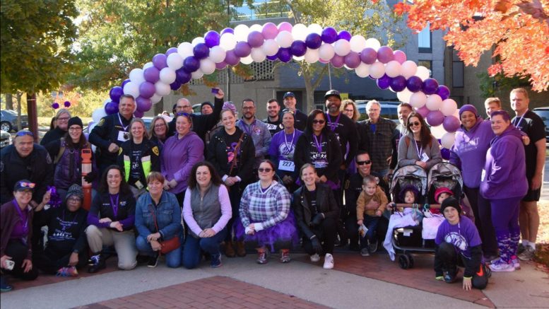 large group photo with everyone posing under a purple and white balloon arch