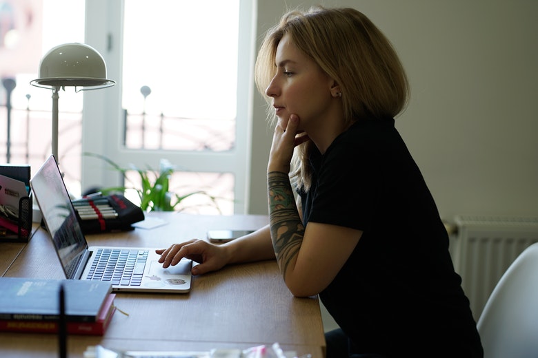 Mulher pensativa mexendo em notebook que está em cima da mesa. Estaria ela fazendo code review de CSS?