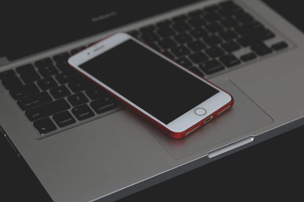 9 regras para web design responsivo: celular branco de bordas vermelhas colocado em cima de um notebook cinza.