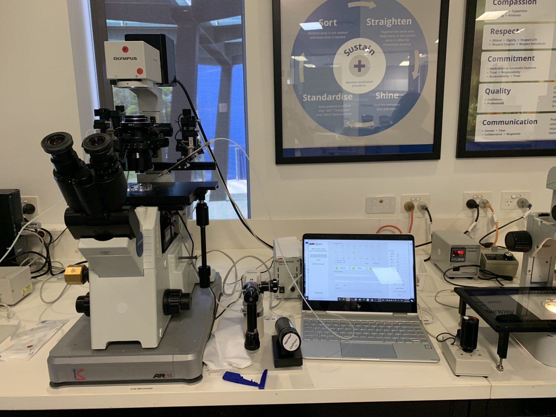 Laboratory microscope setup with a connected laptop displaying data, surrounded by additional equipment on a research bench
