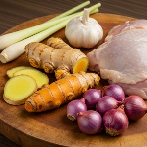 A close-up shot of the key ingredients for Soto Ayam: turmeric, ginger, lemongrass, garlic, shallots, and chicken.