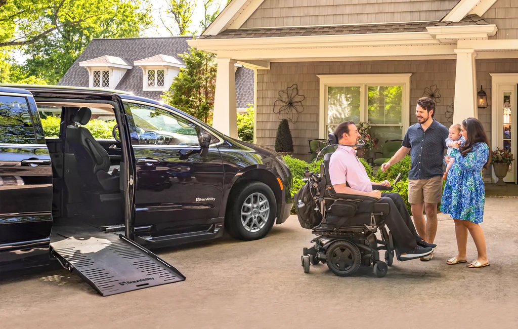 Family greeting a power wheelchair user beside a BraunAbility Chrysler Pacifica