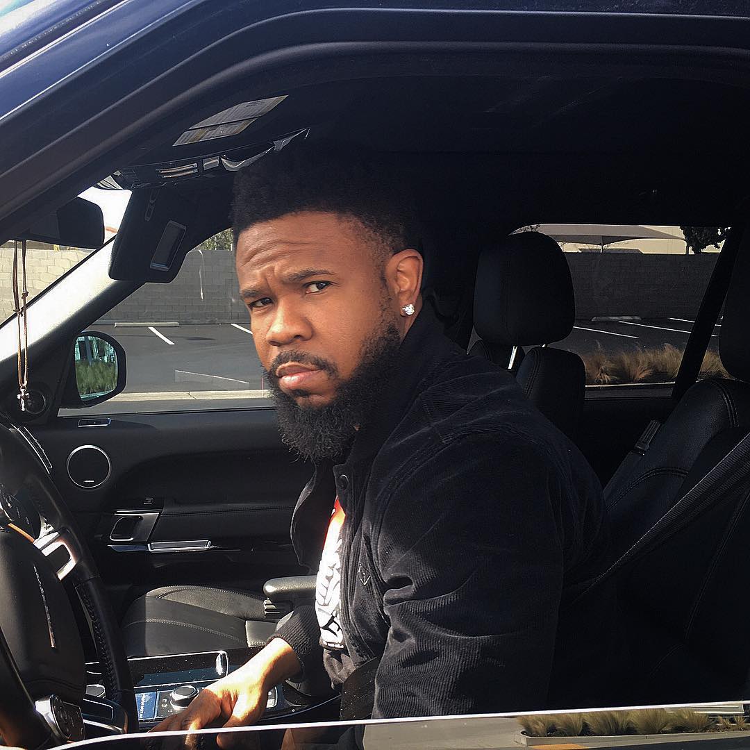 A photo showing American rapper Chamillionaire sitting in the drivers section of a vehicle and he has on a black jacket.