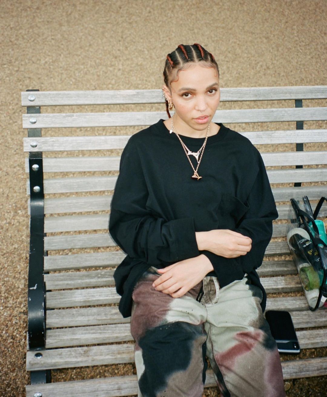 FKA Twigs looks stylish in this patterned pant and black sweatshirt, while sitting on a bench.