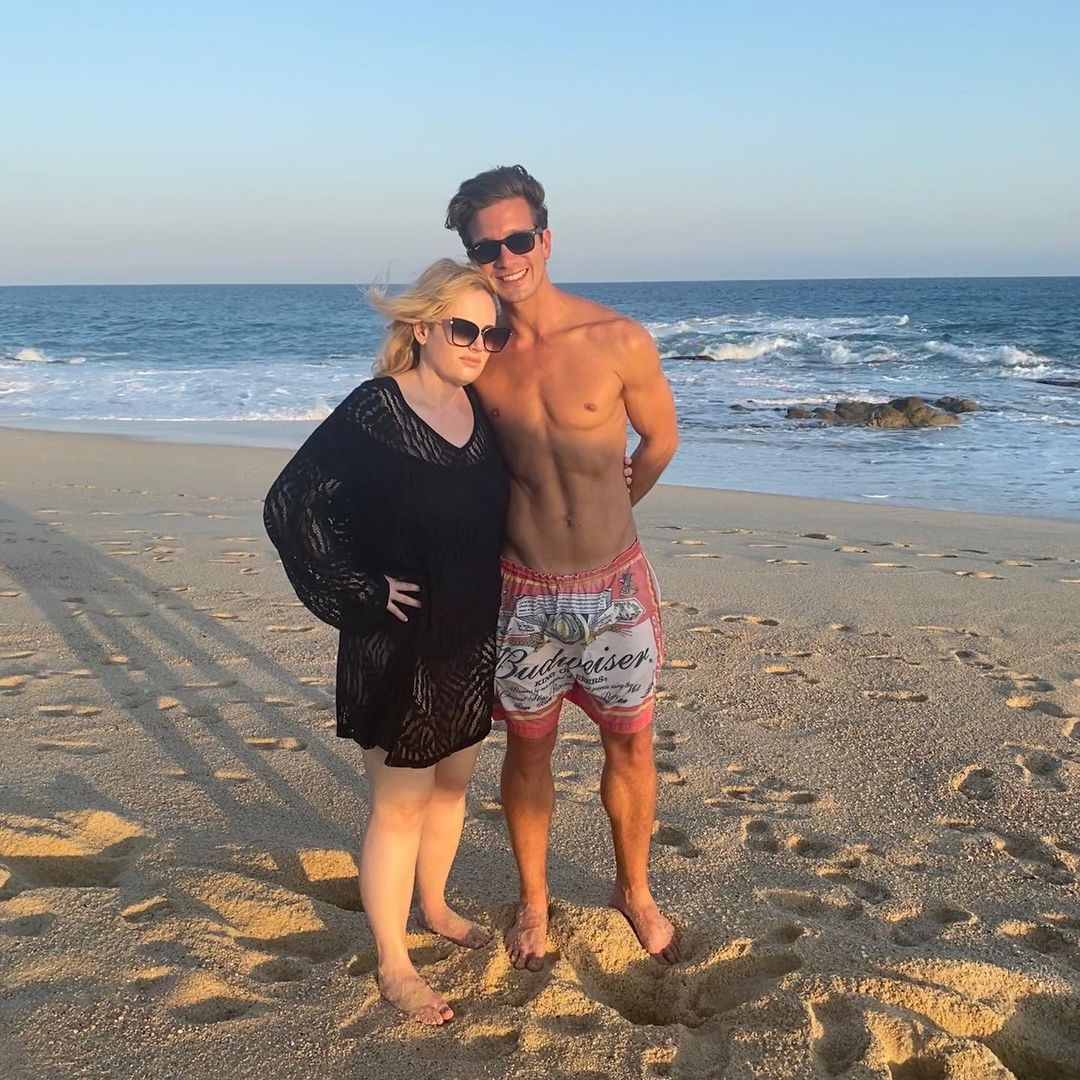 Here, Wilson and Jacob Busch are seen holding each other on the beach with Wilson putting on a black dress and shades and her boyfriend shirtless with a pair of boxers and he also has on shades.