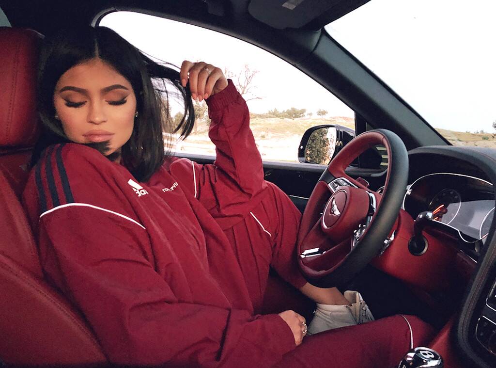 Kylie in a red tracksuit sitting in the drivers seat of a car