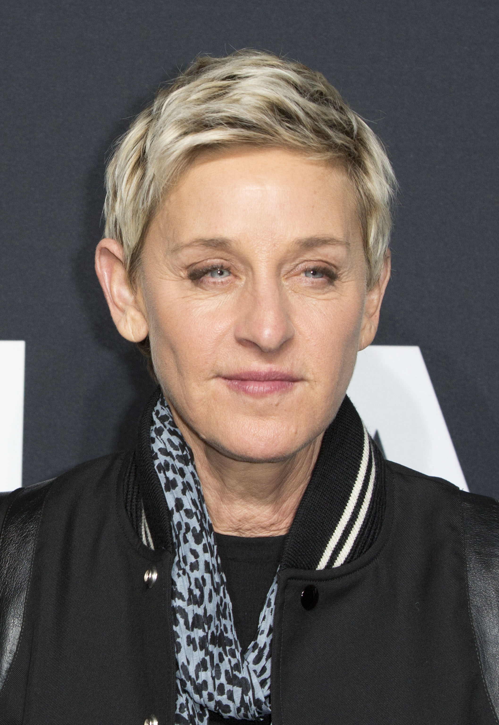 A beautiful photo of Ellen DeGeneres sporting a black jacket and blue scarf with black designs around her neck.