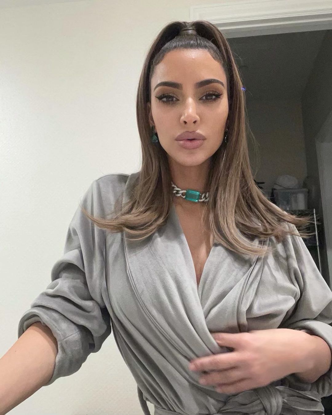 A photo of Kim Kardashian in a gray robe, while striking a pose with pouted lips facing the camera.